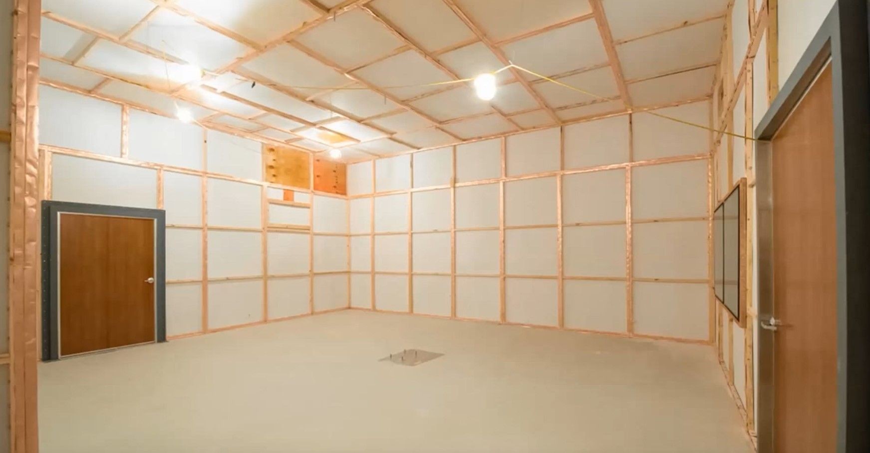 Empty room with beige walls featuring copper framing, two wooden doors, and ceiling lights.