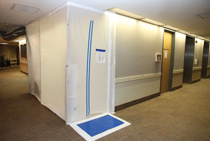 A plastic enclosed area with a taped entrance in a hallway under renovation or construction.